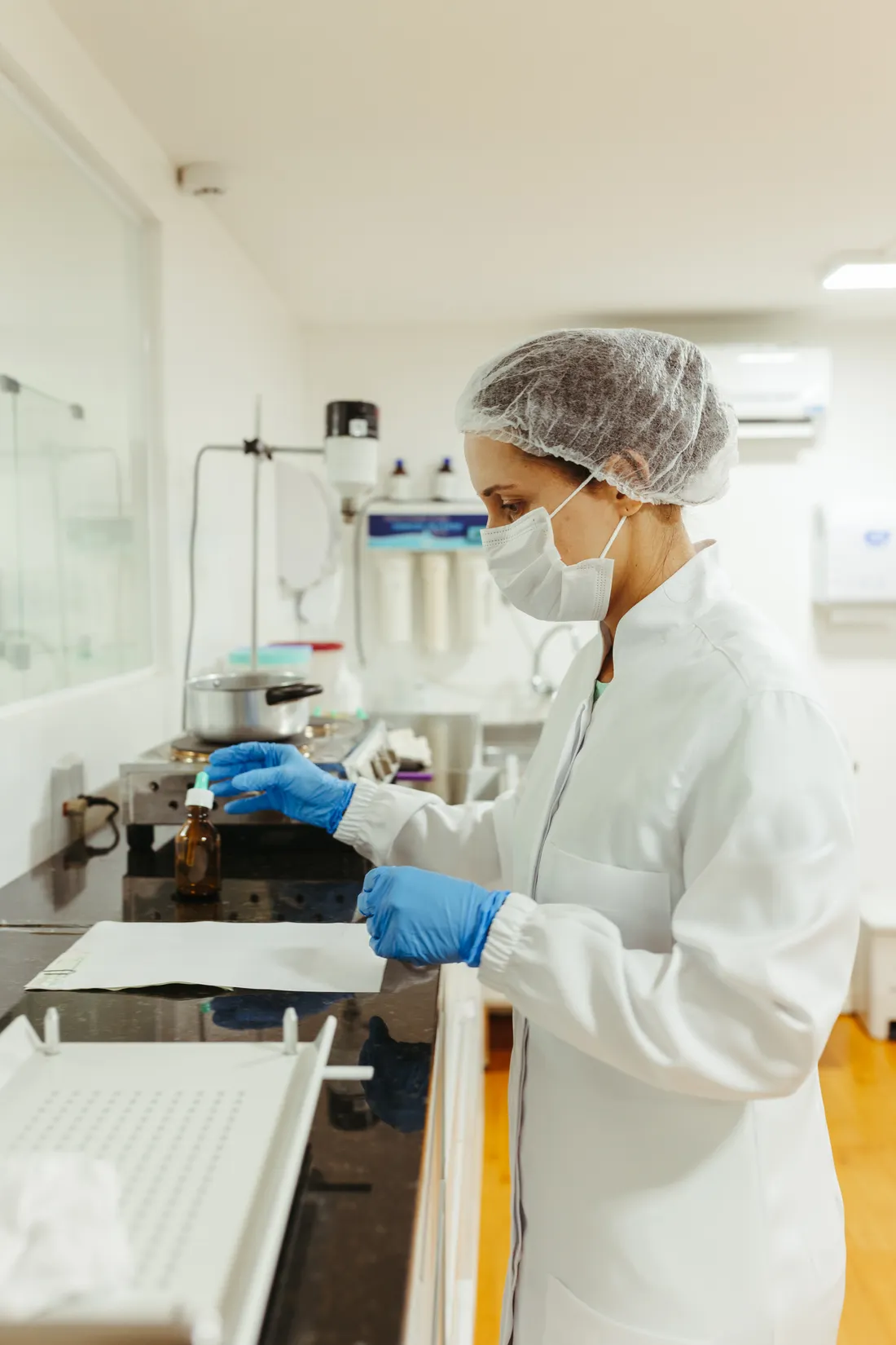 Una técnica de laboratorio con cofia y guantes trabaja en la mesada